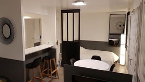 Une chambre d’hôtel de taille réduite, comprenant un lit, un petit bureau avec une chaise, un miroir et un téléviseur fixé au mur.