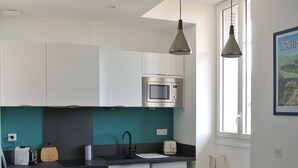 Una cucina moderna con mobili bianchi, un piano di lavoro nero, un forno a microonde e una finestra con persiane.