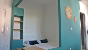 Una stanza compatta con un letto, un piccolo tavolo in legno e una scaffalatura.