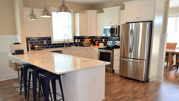 A kitchen with white cabinets, a stainless steel refrigerator, a microwave, a stove, and a large island with bar stools. - Moana & Ohana - Walk to beach in Surfside Beach, SC (Surfside Beach)
