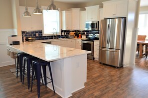 A kitchen with white cabinets, a stainless steel refrigerator, a microwave, a stove, and a large island with bar stools.