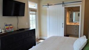 A bedroom with a bed, dresser, TV, sliding door, and a bathroom visible through the door. - Moana & Ohana - Walk to beach in Surfside Beach, SC (Surfside Beach)