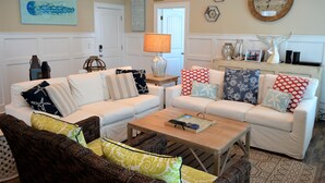 A living room with a white sofa set, a wooden coffee table, and a wicker chair. - Moana & Ohana - Walk to beach in Surfside Beach, SC (Surfside Beach)