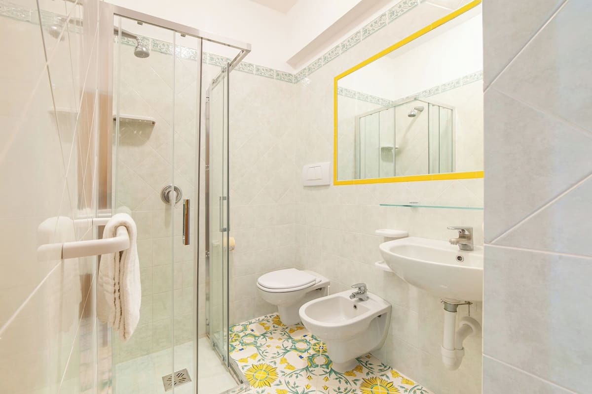 A bathroom with a glass shower enclosure, a toilet, a bidet, and a sink with a mirror.