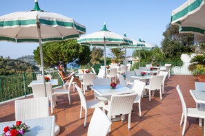 Een terras buiten met witte rieten meubels, groen gestreepte parasols en potplanten.