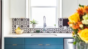 Een keuken met een raam, een spoelbak en een aanrecht met een bloempot en een mand.