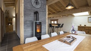 Une cuisine moderne avec un mur en pierre, un poêle à bois et un coin repas agrémenté d’une longue table en bois.