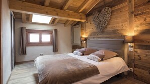 Une chambre avec un plafond en bois, un lit doté d’une tête de lit, une fenêtre avec des rideaux et un luminaire fixé au mur.