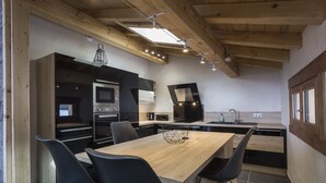 Une cuisine moderne avec une table à manger en bois, des chaises noires et des appareils électroménagers intégrés.