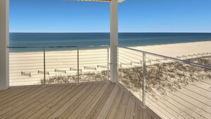 Eine Holzterrasse mit Blick auf einen Sandstrand und das Meer.