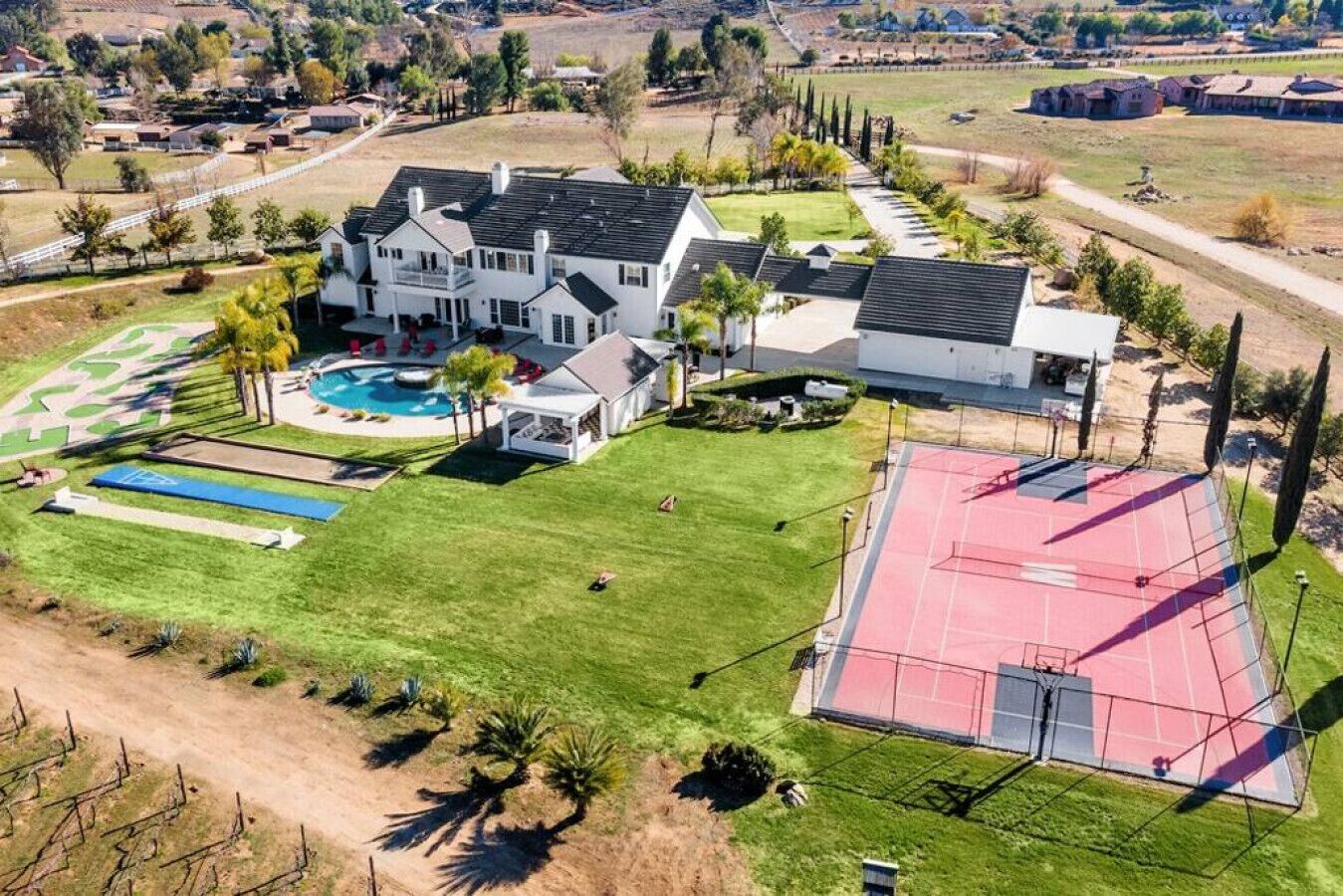 A large house with a swimming pool, tennis court, and a fenced area.