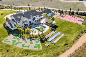 Eine Vogelperspektive eines großen Hauses mit Schwimmbad, Tennisplatz und angelegtem Garten.