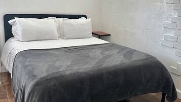 A bed with a dark gray blanket, white pillows, and a black metal frame. There is a wooden nightstand beside the bed.