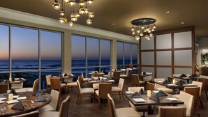 A restaurant with tables and chairs arranged for dining, large windows offering a view of the ocean, and hanging light fixtures. - Exquisite Ocean View-2003 Brighton-Amenity Access (Myrtle Beach)