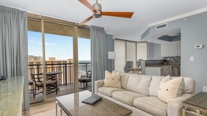 A modern living room with a glass coffee table, beige sofa, and a ceiling fan. - Exquisite Ocean View-2003 Brighton-Amenity Access (Myrtle Beach)