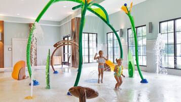Un espace de jeux aquatiques avec des structures colorées en vert et en jaune, une pancarte indiquant « Kingston Plantation », et une grande fenêtre en arrière-plan.