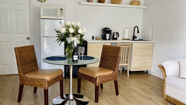 Ett kompakt kök med kylskåp, mikrovågsugn och kaffebryggare. Här finns också en matplats med ett runt bord och två fåtöljer i rotting.