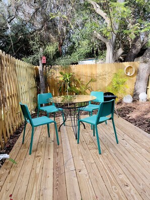 Une terrasse en bois avec une table en verre et quatre chaises de couleur turquoise.