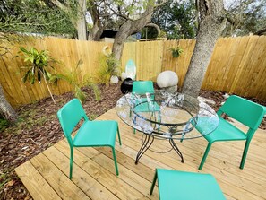 Une terrasse en bois avec une table à plateau de verre et quatre chaises vertes.