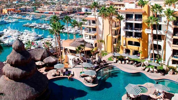 Un resort con un amplio área de piscina, numerosas tumbonas y un puerto deportivo con barcos.