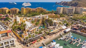 Zona turística costera con varios edificios, un puerto deportivo y un gran crucero al fondo.