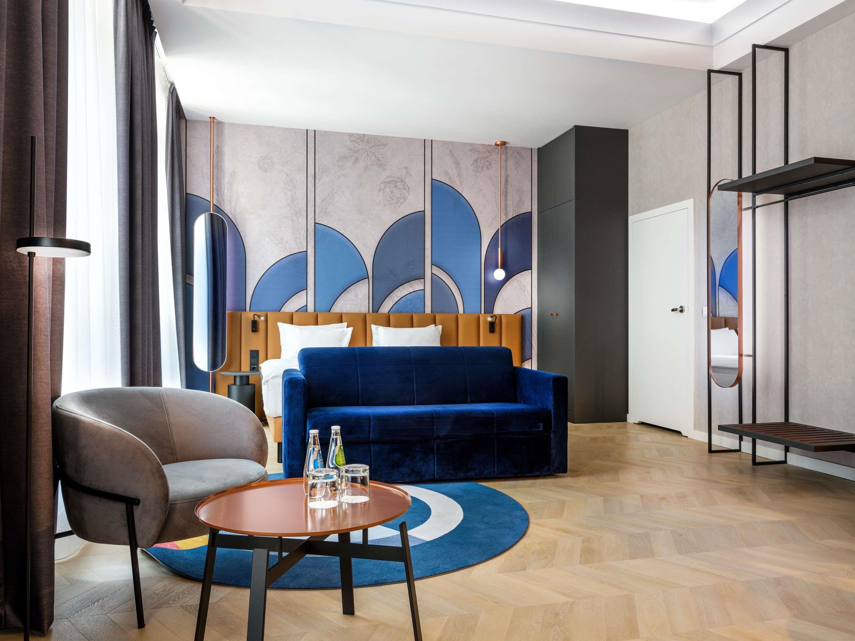 Ein modernes Hotelzimmer mit einem Bett, einem blauen Sofa, einem runden Holztisch und einem Stuhl.