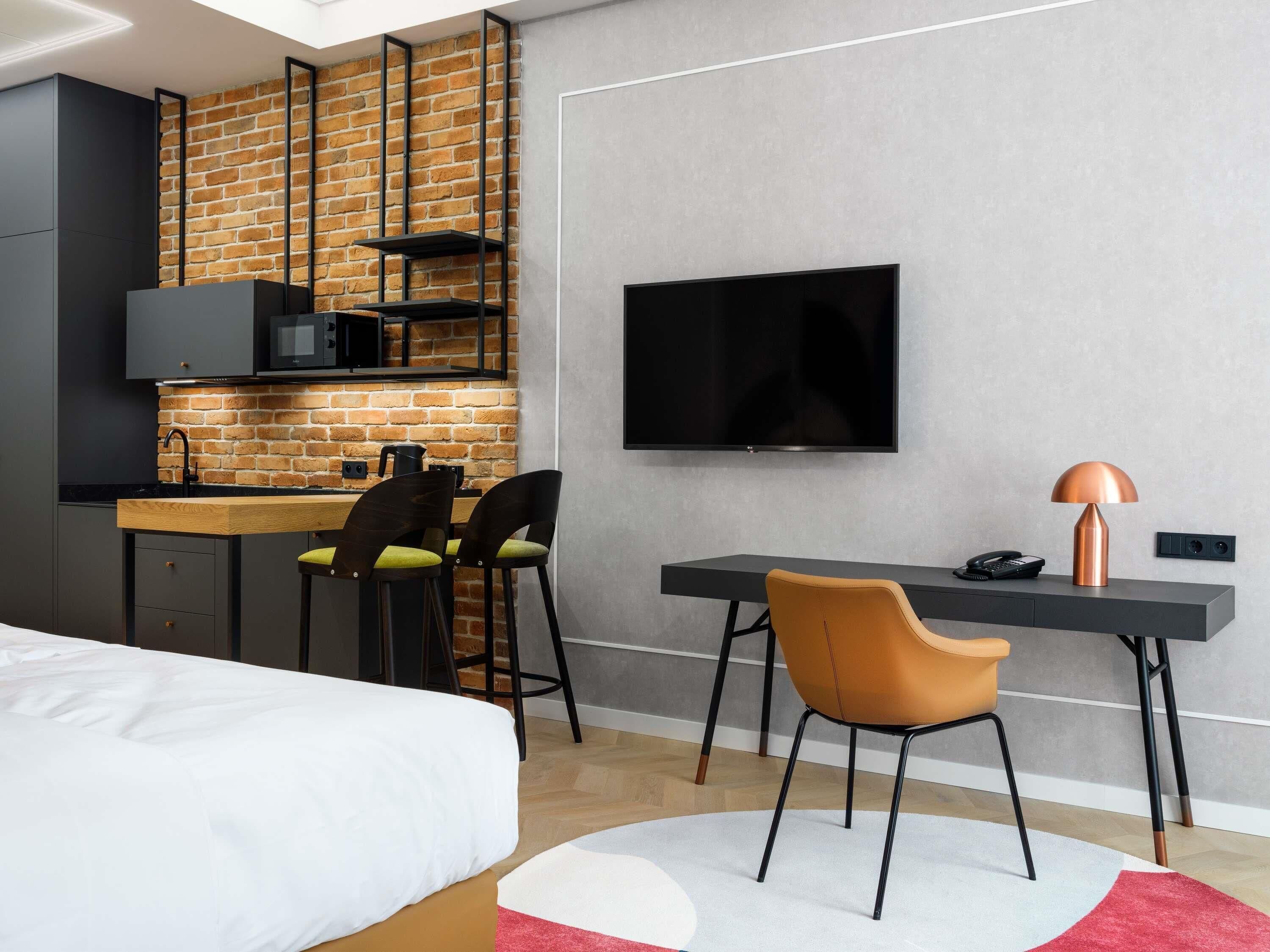Ein modernes Hotelzimmer mit Küchenzeile, einem Bett, einem Schreibtisch mit Stuhl und einem Fernseher.