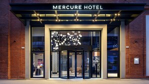 Exterior del Hotel Mercure con entrada de vidrio, señalización iluminada y diseño moderno.