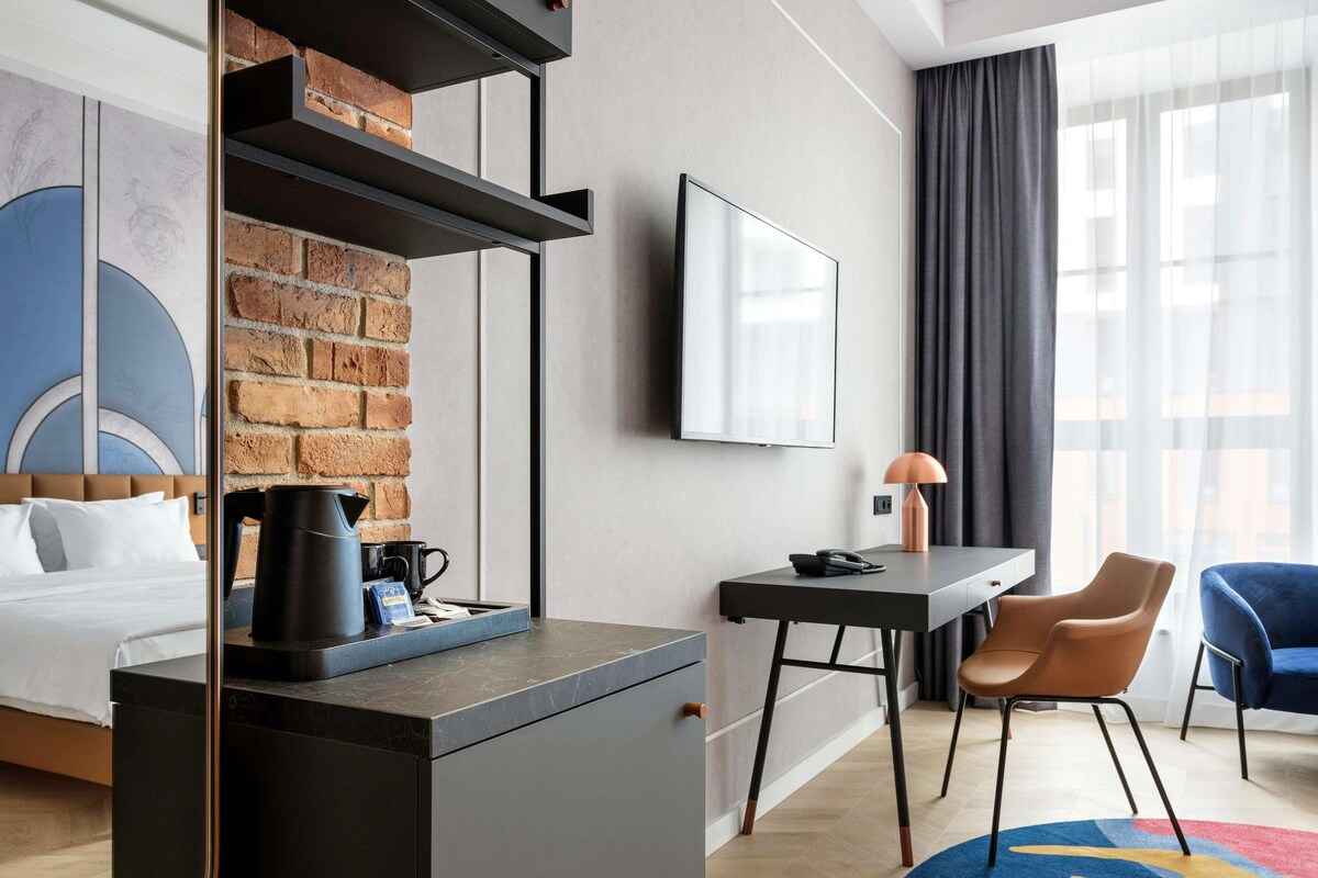 Une chambre d’hôtel moderne équipée d’un lit, d’un bureau, d’une machine à café, d’une chaise et d’un téléviseur.