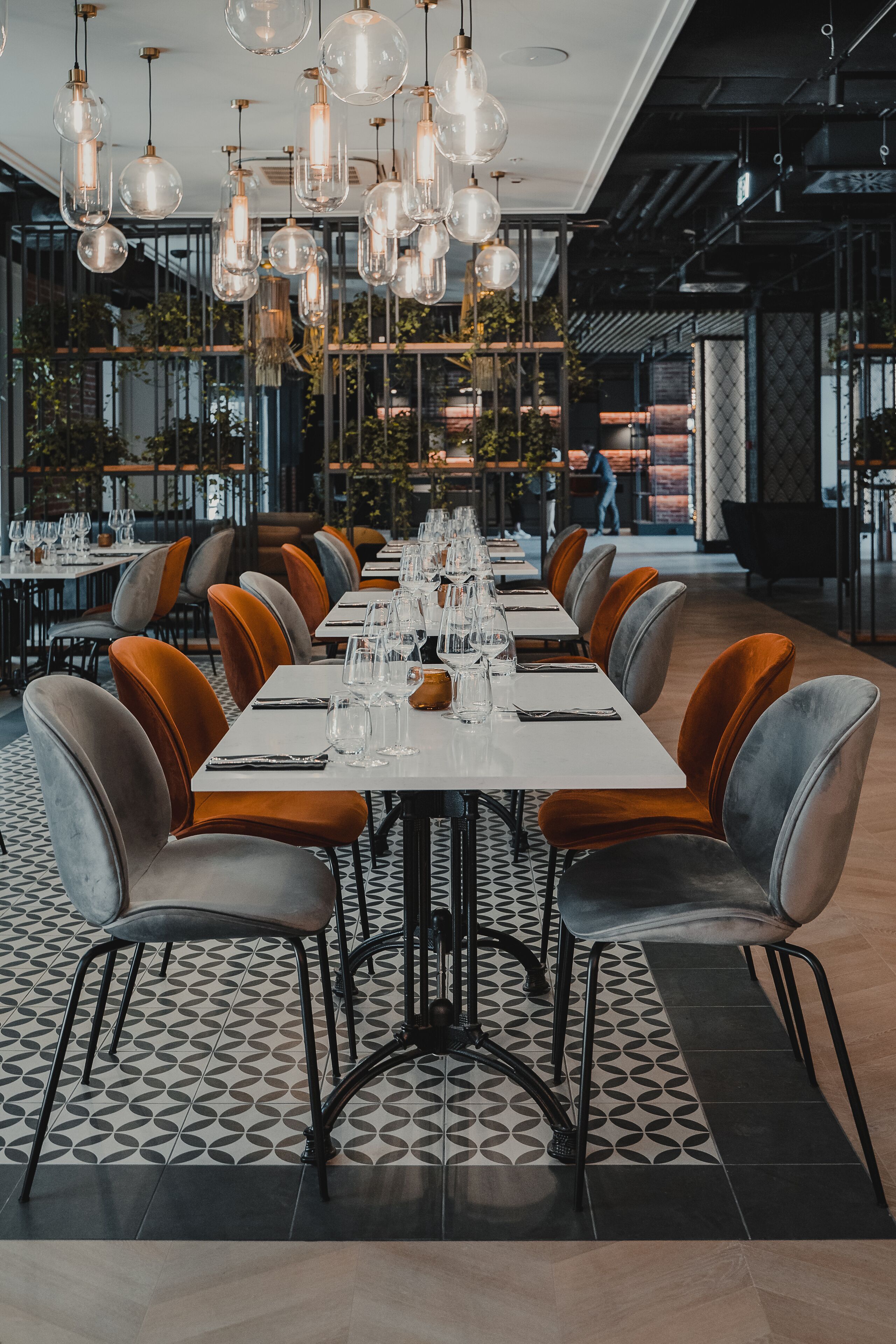 A modern restaurant with a long dining table set for a meal, surrounded by upholstered chairs.