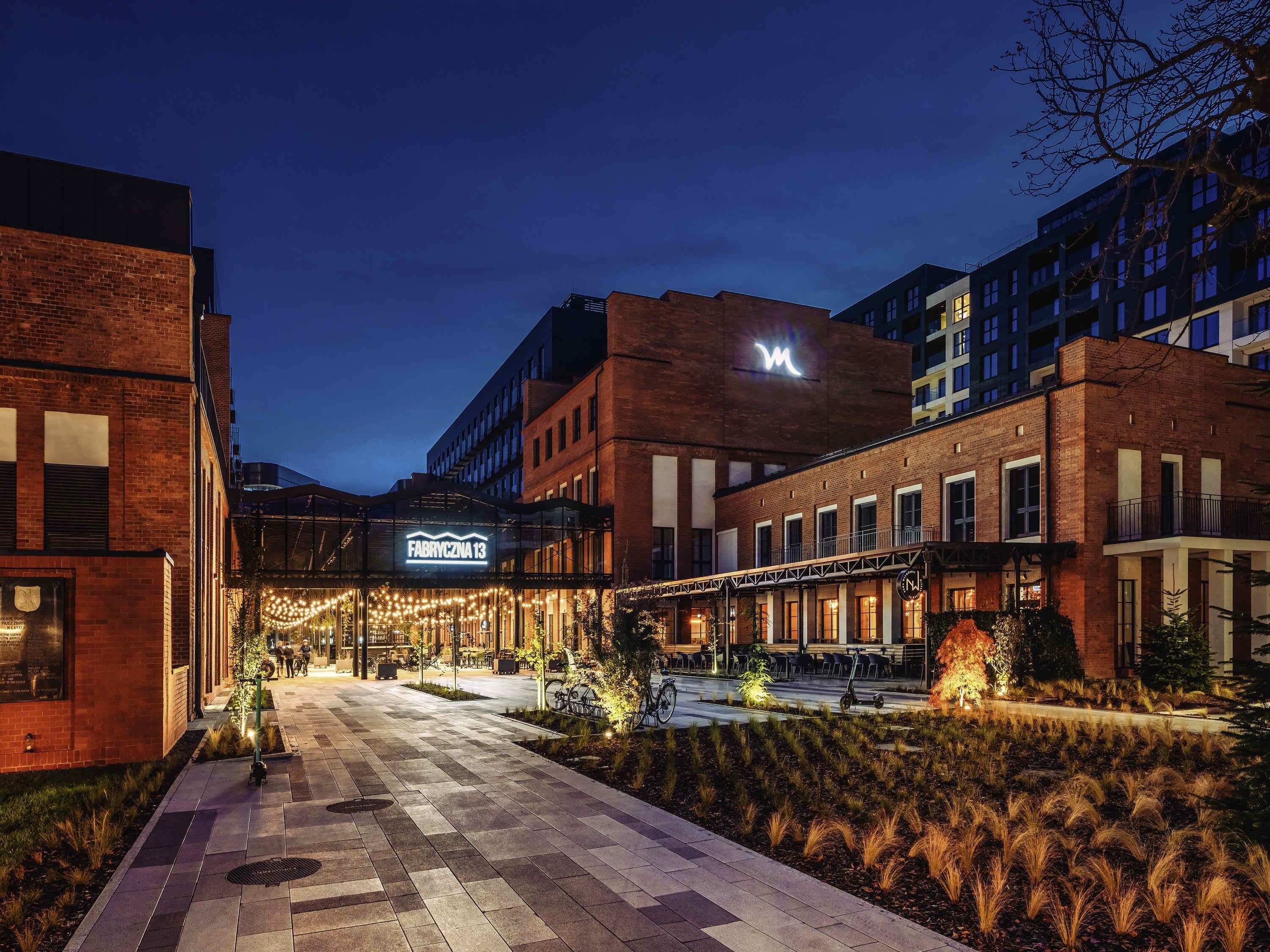 Hotel de diseño moderno, con fachadas de ladrillo y vidrio, un área exterior bien iluminada con asientos y un cartel llamativo del hotel.