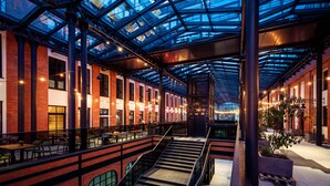 Un amplio espacio interior con techo de cristal, paredes de ladrillo y una escalera central.