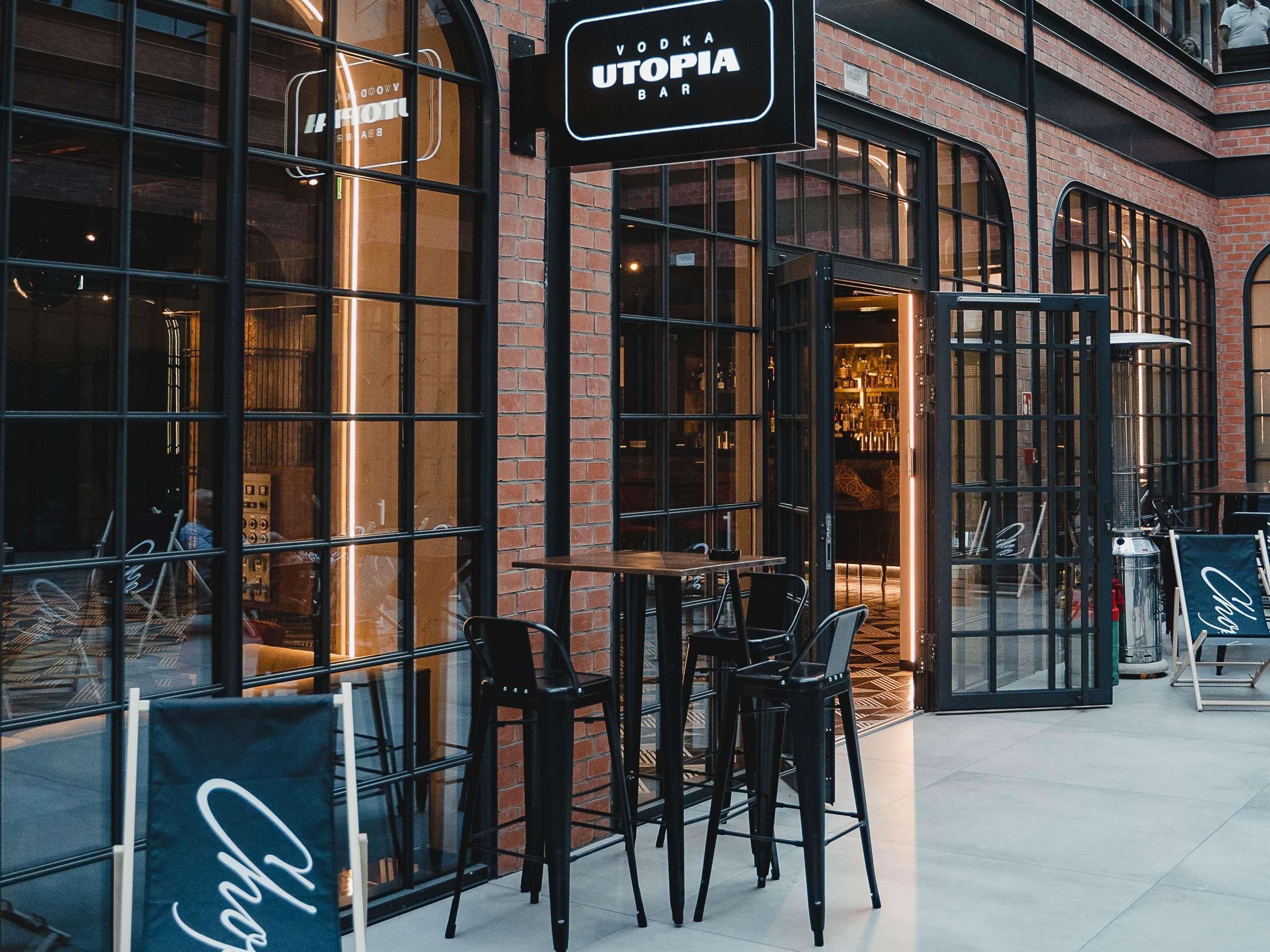 Un bar llamado UTOPIA, con grandes ventanales y fachada de ladrillo.