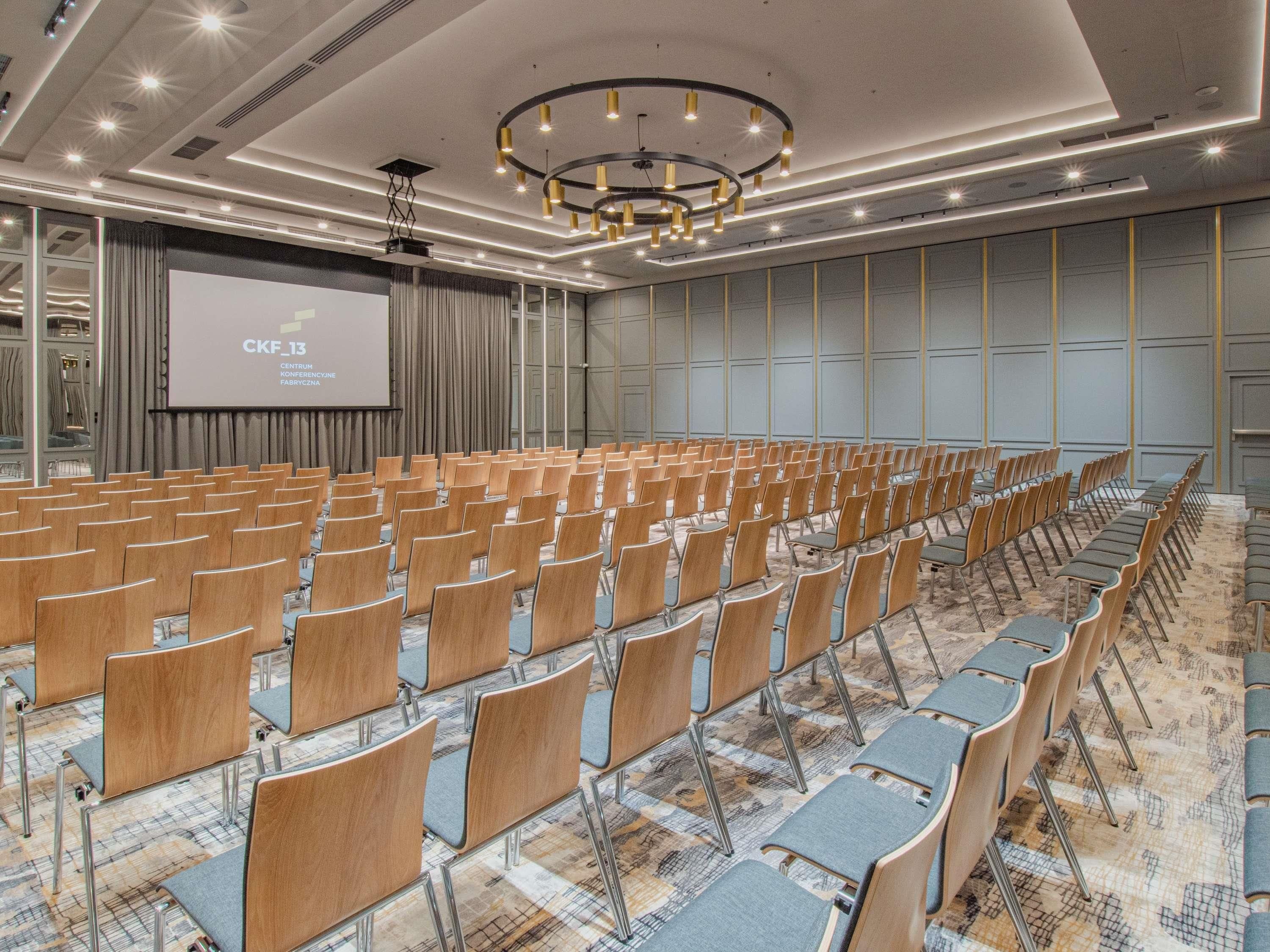 A conference room with rows of chairs, a projector screen, and a modern chandelier.
