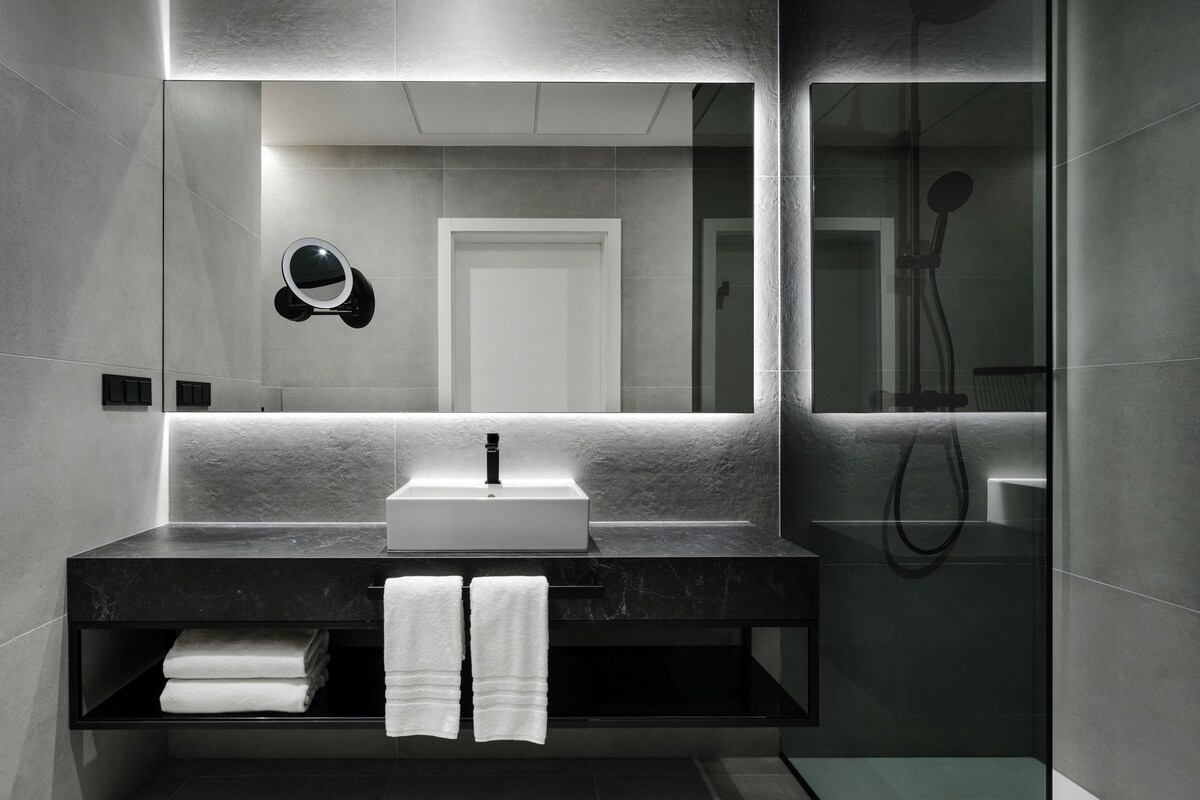 Une salle de bain moderne avec un grand miroir, un lavabo et un espace douche.