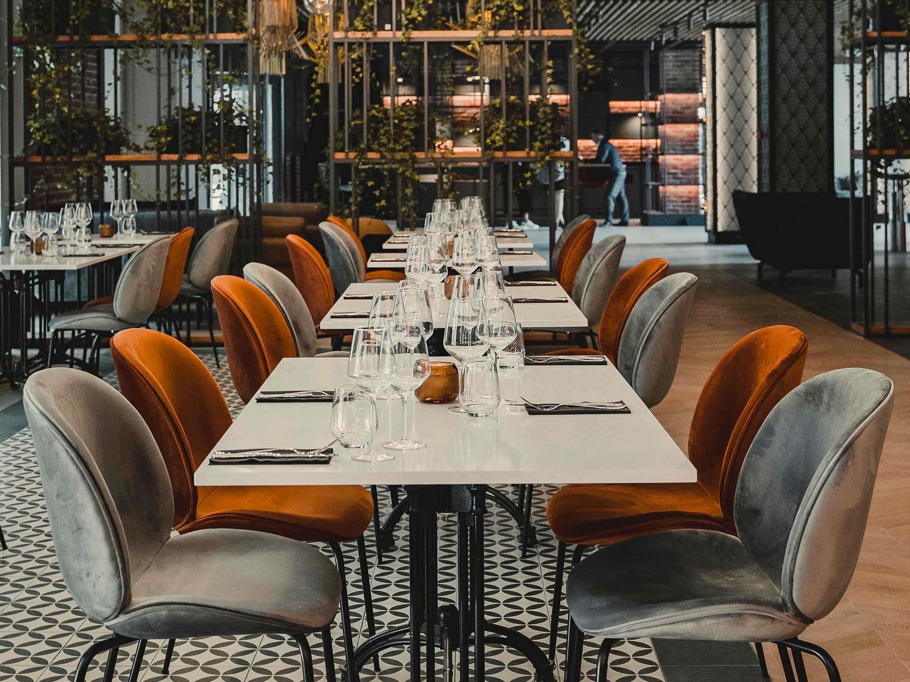 A restaurant with long tables set for dining, surrounded by upholstered chairs.