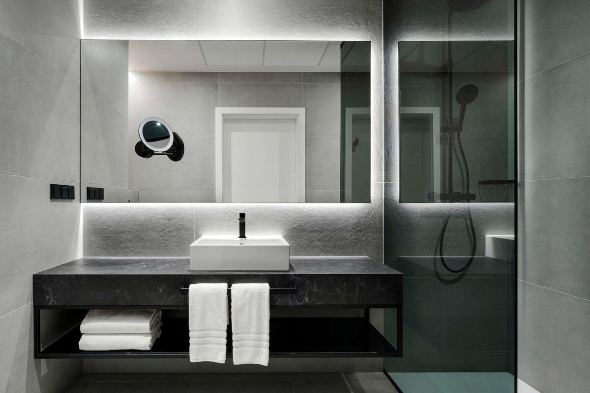 Une salle de bain moderne avec un grand miroir, un lavabo et un espace douche.