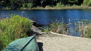 En kanot ligger vid en sandstrand vid en stilla sjö, med en tät skog i bakgrunden.