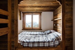 Ein gemütliches Schlafzimmer mit Holzbalkendecke, einem großen Fenster mit Bergblick und einem Bett mit karierter Bettwäsche.
