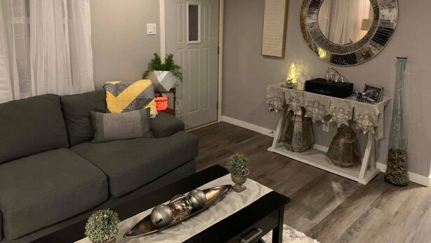 Un salon avec un canapé gris, une table basse agrémentée d’objets décoratifs, une table d’appoint avec une lampe, et un miroir au mur.