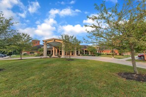 A building with a covered entrance, a lawn, and trees.