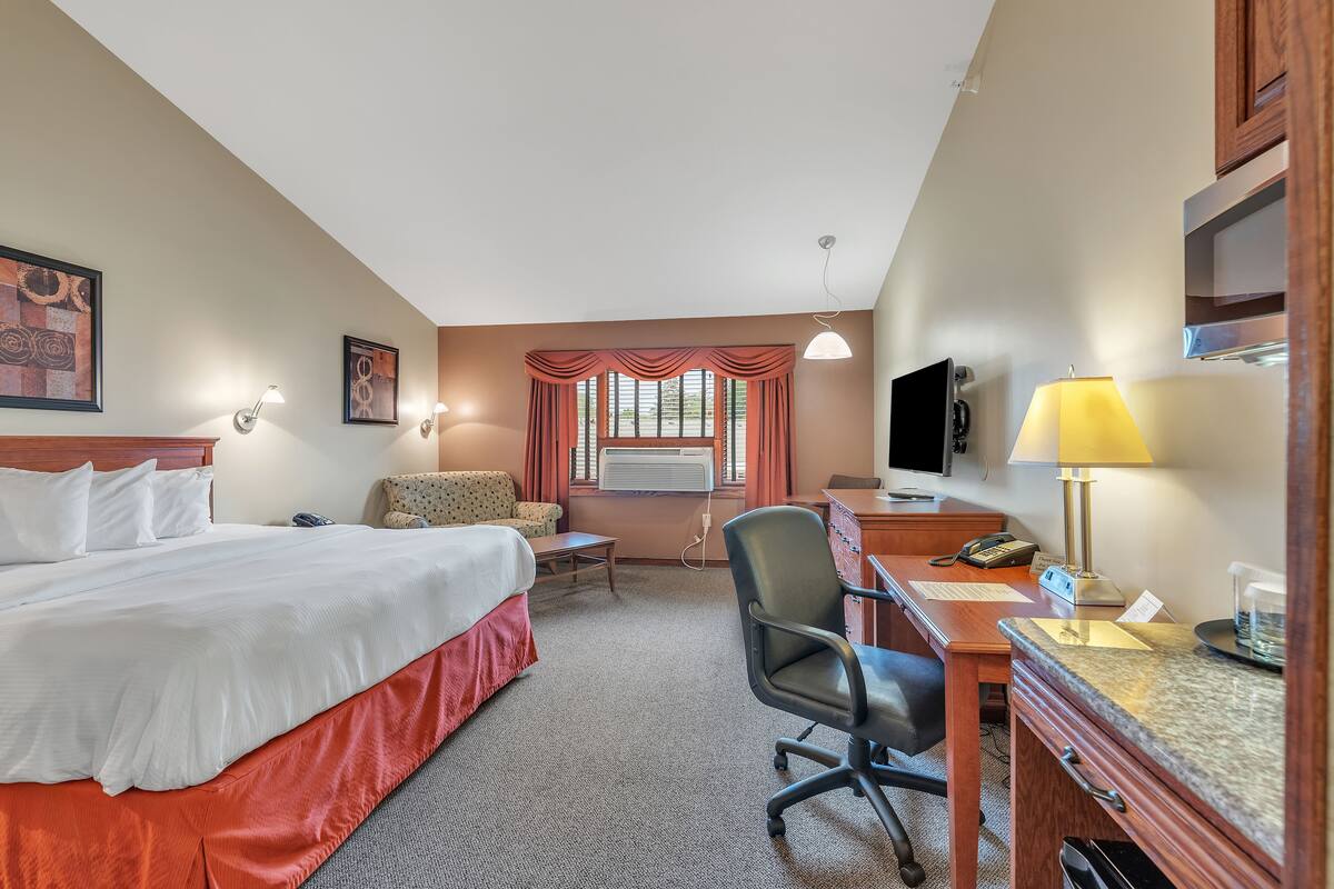 Ein Hotelzimmer mit Bett, Schreibtisch, Stuhl, Fernseher und einem Fenster mit Vorhängen.