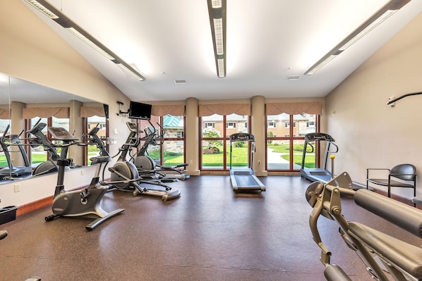A gym with exercise equipment, large windows, and a view of the outside.