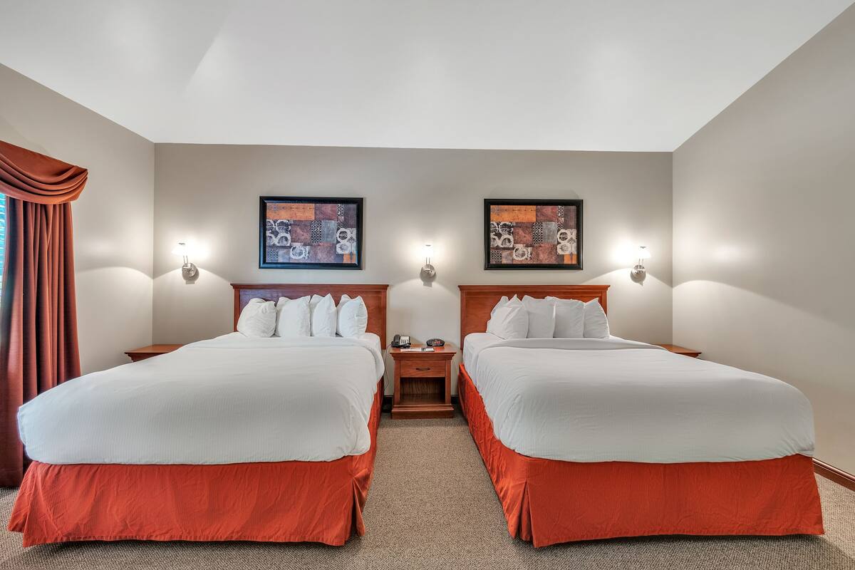 Ein Hotelzimmer mit zwei Betten, einem Nachttisch, einer Lampe und Bildern an der Wand.