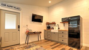 A modern kitchen with a flat-screen TV, a black refrigerator, and wooden cabinets. - Barnside Hangout - Ranch Retreat - Master Spa - Hot Tub - Near Fredericksburg (Fredericksburg)