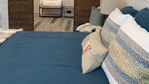 A bedroom with a bed, pillows, a wall-mounted air conditioner, and a door leading to another room. - Barnside Hangout - Ranch Retreat - Master Spa - Hot Tub - Near Fredericksburg (Fredericksburg)