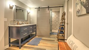 A modern bathroom with a dark vanity, a large mirror, and a wooden ladder shelf. - Barnside Hangout - Ranch Retreat - Master Spa - Hot Tub - Near Fredericksburg (Fredericksburg)
