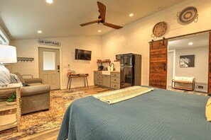 A bedroom with a bed, a desk, a chair, a ceiling fan, a refrigerator, and a door labeled "OUR HAPPY PLACE". - Barnside Hangout - Ranch Retreat - Master Spa - Hot Tub - Near Fredericksburg (Fredericksburg)