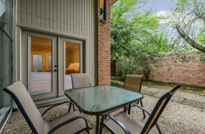 Relax in this outdoor seating area with a glass-top table and comfortable chairs, surrounded by a brick wall and lush greenery.