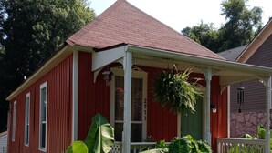 Ein rotes Haus mit Veranda, davor große, grüne Pflanzen und ein Briefkasten.